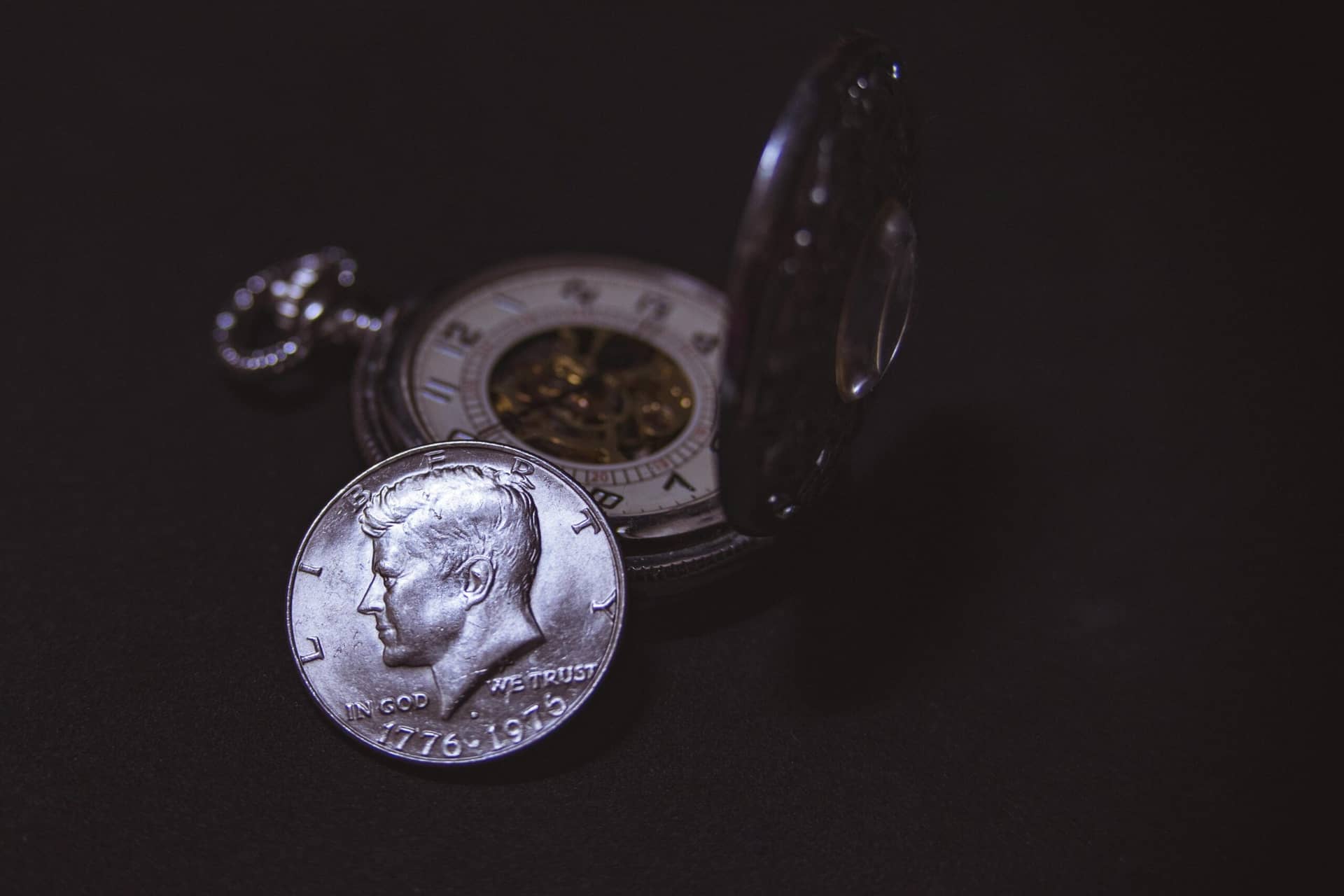 Close-up of a vintage silver coin with a pocket watch, symbolizing time and wealth.