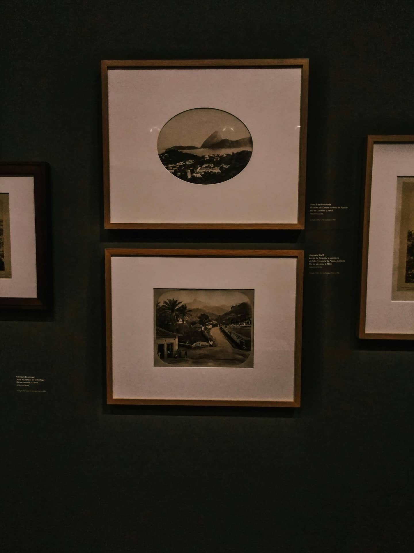 A collection of framed art prints on a dark wall in a gallery setting.